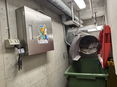 A Garbage Doctor 3000 on the bin room wall beside a garbage chute, above a green bin