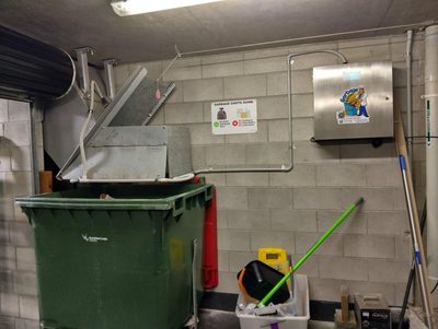 A Garbage Doctor on a block wall beside a chute hopper and its bins